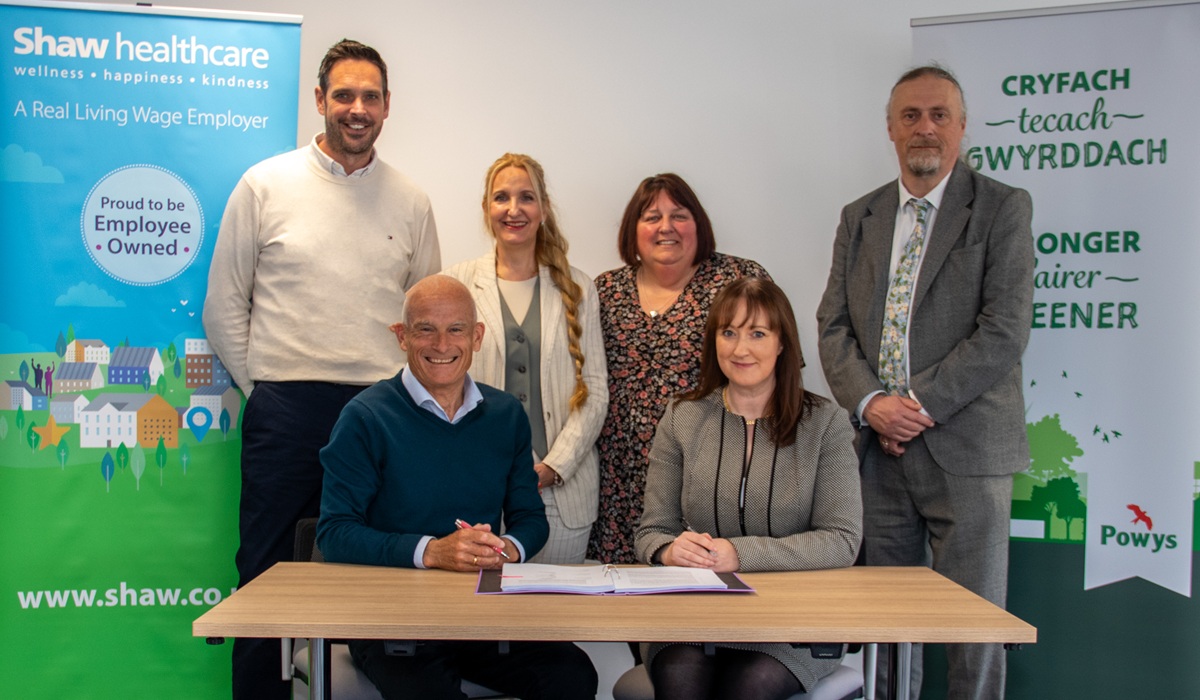 Russell Brown, Shaw Healthcare's Chief Executive Officer and Nina Davies, Powys County Council's (PCC) Director of Social Services and Wellbeing signing the new 15-year contract. With them are back row, from left to right: Geraint Evans, Shaw's Operations Director; Rachel Evans, PCC's Senior Strategic Commissioning Manager; Sharon Frewin, PCC's Head of Adult Services; and Peter Lathbury, Strategic Commissioning Manager – Age Well.