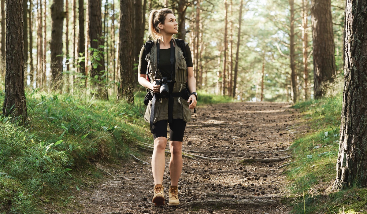 Woman hiker walking with a backpack and modern mirrorless camera